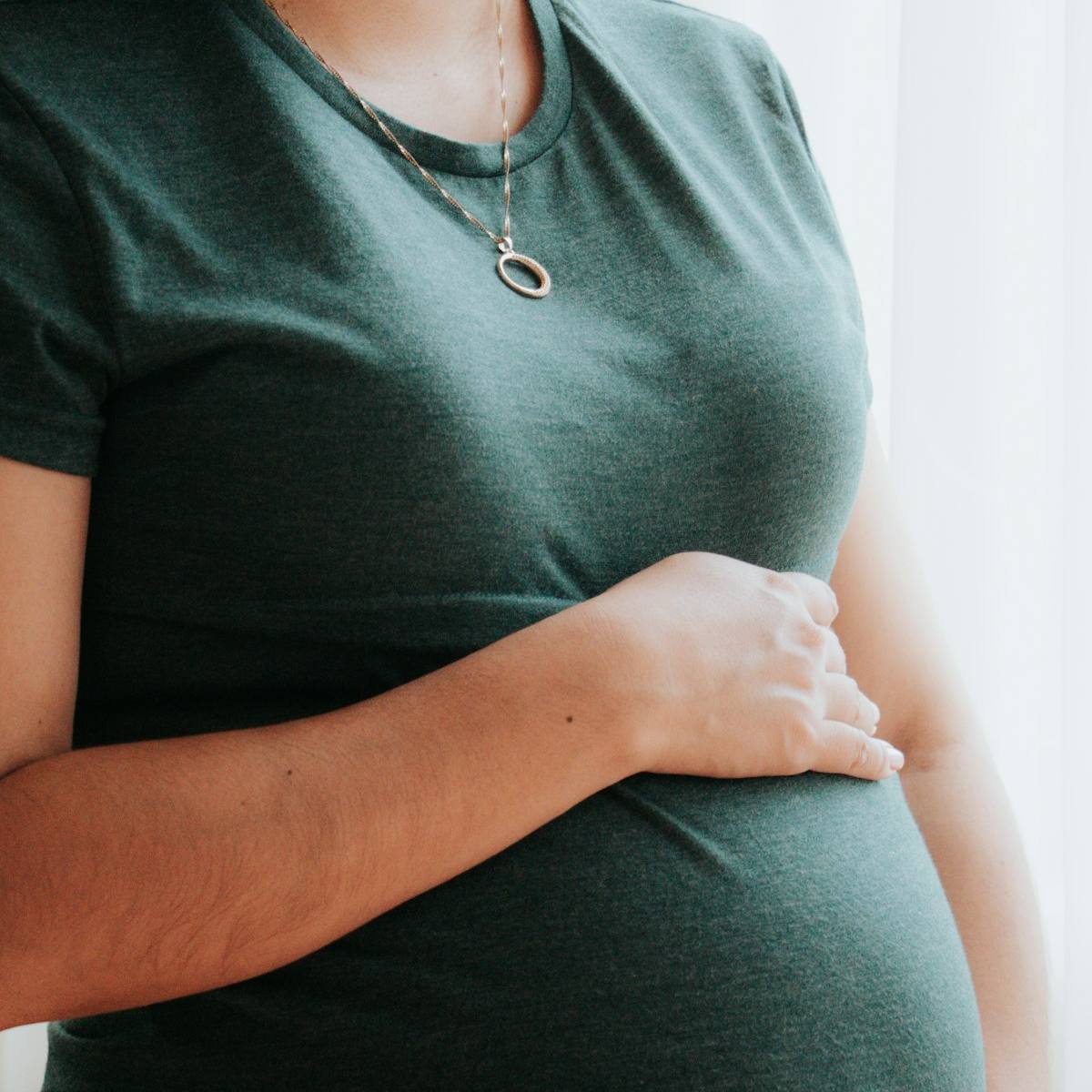 Femme enceinte debout près d'une fenêtre, baignée d'une lumière douce.