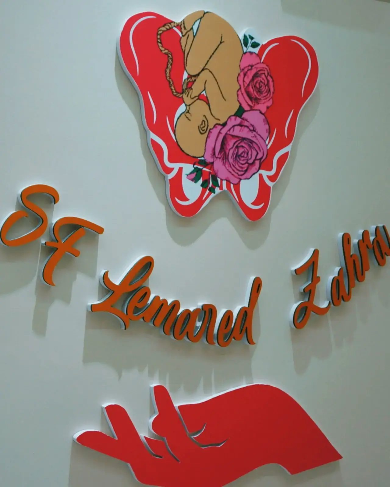 Enseigne peinte à la main sur le mur du cabinet : un cœur, des roses, le nom « SF Lemared Zahra » en lettres cursives.